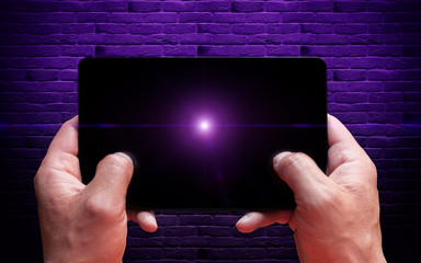 Computer tablet in male hands close-up, top view. Neon light, magic. Brick wall background