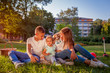 © maryviolet - Happy family spending time outdoors sittting on grass in park. Mom with two children smiling. Family values