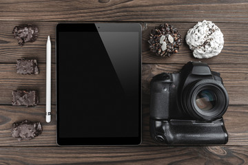 Workspace with tablet PC, camera and biscuits on wooden table. View from above, office table desk