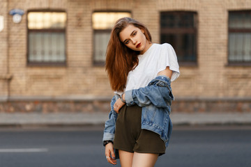 Canvas Print - Fashionable beautiful woman in a denim vintage jacket with a gray t-shirt standing near a road on the street