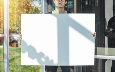 Close up of young attractive man holding blank canvas at metro station.