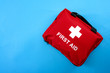 © Victor Moussa - First aid treatment and medical emergency response concept with flat lay view of a red with a white cross first aid kit isolated on blue background with copy space for text