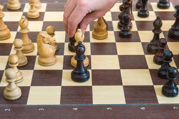 Hand moving a wooden chess figure on a chess board