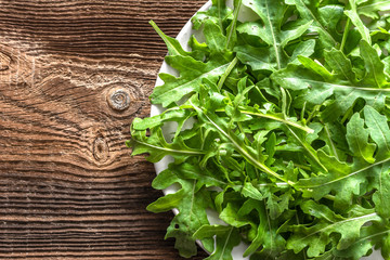 Wall Mural - Fresh arugula leaves on plate on wooden table, healthy food concept