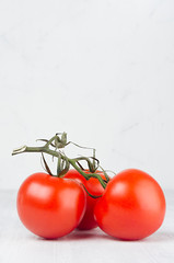 Wall Mural - Pulpy red tomatoes on branch in light soft white modern kitchen interior with copy space, vertical, closeup.