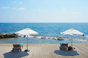 Rest on the tropical coast. Umbrellas and two empty lounge chairs stand on a wooden deck near the sea