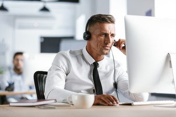 Wall Mural - photo of caucasian man 30s wearing office clothes and headset, sitting by computer in call center