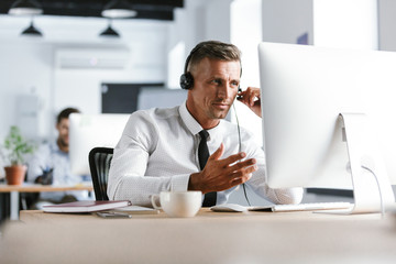 Wall Mural - photo of businesslike man 30s wearing office clothes and headset, sitting by computer in call center