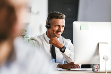 Wall Mural - photo of handsome man 30s wearing office clothes and headset, working on computer in call center
