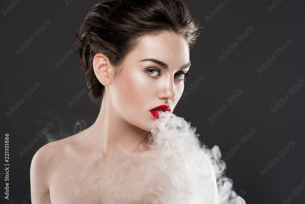 beautiful nude woman vaping and blowing smoke, isolated on grey Stock