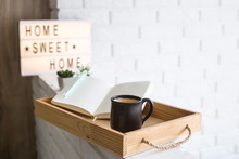 A Cup Of Coffee And An Open Notebook On A Wooden Tray In The Bright Interior Of The Apartment. Home Sweet Home Written On A Decorative Frame