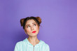 © Drobot Dean - Portrait of european brunette girl with two buns looking upward on copyspace and twisting mouth, isolated over violet background in studio