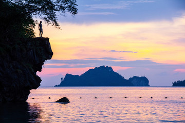 Wall Mural - Woman jumping over a cliff into the sea on sunset in Railay.