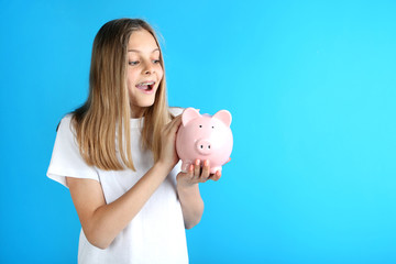 Wall Mural - Young girl with piggy bank on blue background