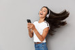 © Drobot Dean - Emotional woman using mobile phone listening music with headphones isolated over grey background.
