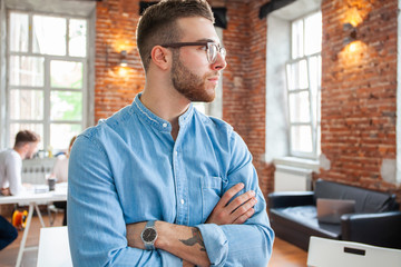 Canvas Print - Handsome businessman is looking out the window and smiling while standing in office.