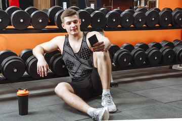 Sticker - Handsome athletic man using mobile phone, surfing internet social network in gym. Guy with towel resting after exercise in fitness center