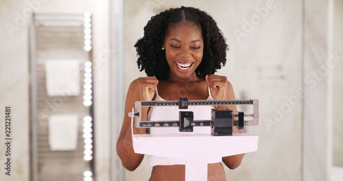 Fotografía Beautiful black woman happily weighs herself on scale in bathroom
