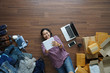 Top view smiling asian woman laying on wooden floor and writing in note book, Selling online start up small business owner SME idea concept