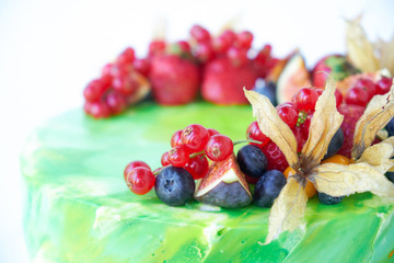 Wall Mural - Cake with whipped green cream, decorated with fresh strawberries, blueberries, figs and physalis on white background. Picture for a menu or a confectionery catalog. Close up.