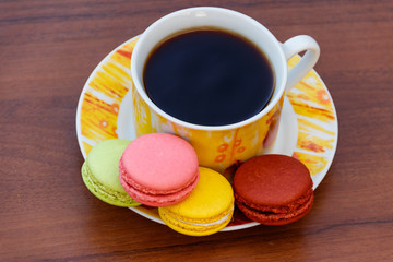 Cup of coffee with tasty colorful macarons on wooden table