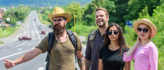 Wall Mural - Travellers try to stop car. Friends hitchhikers travelling summer sunny day. Begin great adventure in your life with hitchhiking. Company friends travelers hitchhiking at edge road nature background