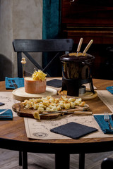 Gourmet fondue with a variety of cheeses on the board along with a warmed pot of cheese fondue.