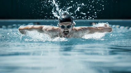 The dynamic and fit swimmer in cap breathing performing the butterfly stroke at pool. The young man. The fitsport, swimmer, pool, healthy, lifestyle, competition, training, athlete, energy concept