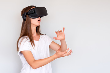 Smiling positive woman wearing virtual reality goggles headset, vr box. Connection, technology, new generation, progress concept. Girl trying to touch objects in virtual reality. Studio shot on gray