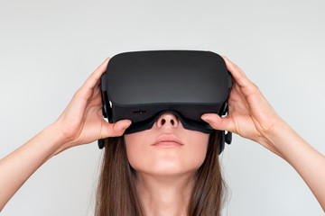 Wall Mural - Young woman wearing virtual reality goggles headset, vr box. Connection, technology, new generation, progress concept. Girl trying to touch objects in virtual reality. Studio shot on gray