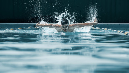 Wall Mural - The dynamic and fit swimmer in cap breathing performing the butterfly stroke at pool. The young man. The fitsport, swimmer, pool, healthy, lifestyle, competition, training, athlete, energy concept