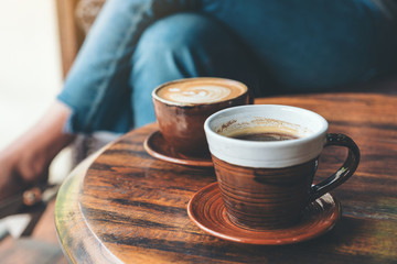 Closeup image of two cups of hot latte coffee and black coffee on vintage wooden table in cafe