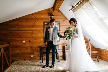 Wall Mural - The groom hold hand bride in white dress are holding a beautiful wedding bouquet flowers, greenery and decorated with ribbon at home. Portrait of a beautiful young couple.