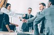 © LIGHTFIELD STUDIOS - multicultural businesspeople shaking hands in conference hall while team leader showing thumb up