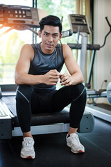 The handsome man is wearing exercise suit,sitting on electric treadmill,with smile and happy face