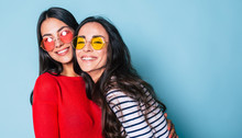 Like A Sisters! Two Beautiful Young Girl Friends In Sunglasses Posing With Smile And Have A Fun On Blue Background