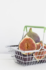 Wall Mural - Fig in a small shopping basket with green handles on a light background