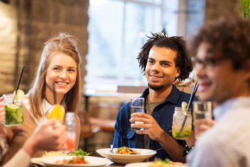 Wall Mural - leisure and people concept - happy friends eating and drinking non-alcoholic drinks at bar or restaurant