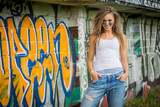 Fototapeta  - Young woman wearing street fashion cloths on graffiti background
