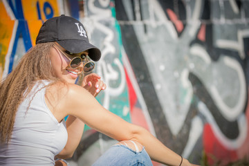 Portrait of young beautiful woman wearing white tank shirt and blue jeans and black hat on brick wall with graffiti background