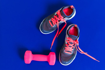 gray sneakers pink laces dumbbell on a blue background