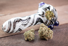 Cannabis Buds On Wood, Beside A Packed Marijuana Pipe