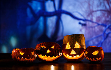 orange pumpkins with scary faces and candles lies on the table in front of dark blue background. Halloween celebration concept