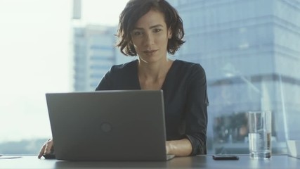 Sticker - Confident Female Executive Works on a Laptop Sitting at Her Desk in Modern Office with Grandiose Cityscape View. Businesswoman Uses Laptop.
