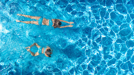 Wall Mural - Aerial drone view of children in swimming pool from above, happy kids swim on inflatable ring donuts, girls have fun in water on family vacation
