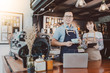 © bunditinay - Young Asian man&woman barista wear apron using laptop with coffee cup served to customer at bar counter in coffee shop with smile face.Concept of cafe and coffee shop small business.
