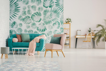 Wall Mural - Pink chair next to blue couch against green wallpaper in spacious flat interior with stool. Real photo