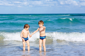 Two happy little kids boys running on the beach of ocean. Funny cute children, siblings, twins and best friends making vacations and enjoying summer on stormy sunny summer day. Miami, Florida