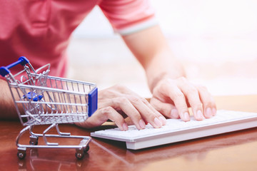 Asian man using laptop next to shopping cart,online shopping concept.