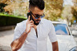 © AS Photo Family - Stylish tall arabian man model in white shirt, jeans and sunglasses posed at street of city. Beard rich attractive arab guy against white suv car, speaking on mobile phone.